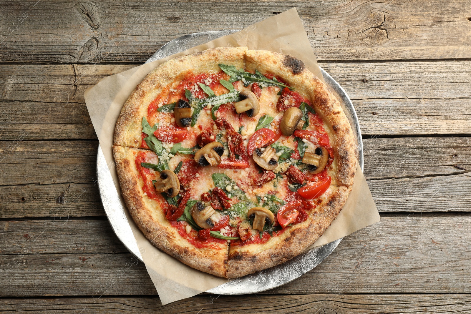 Photo of Tasty pizza with mushrooms, tomatoes and arugula on wooden table, top view