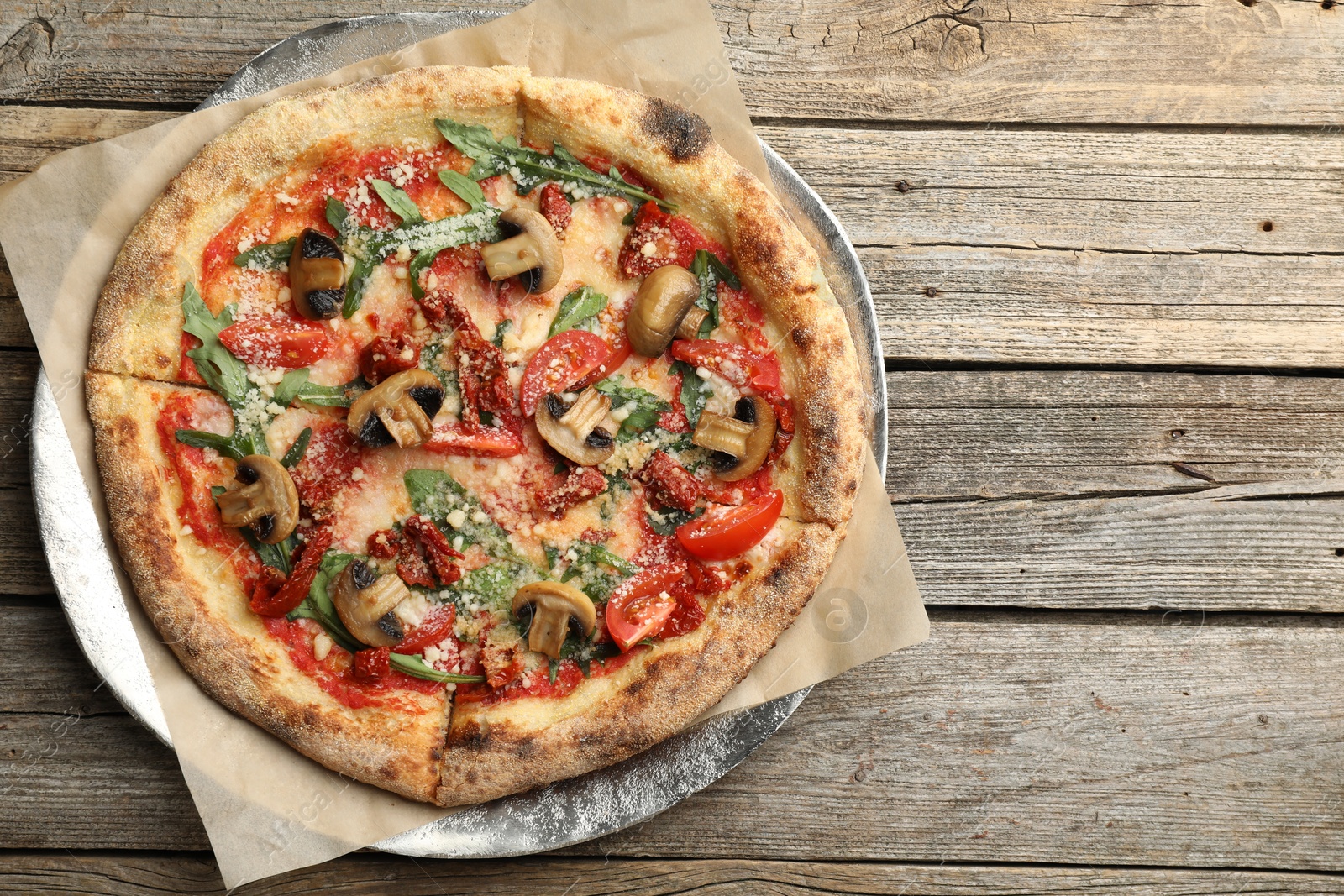 Photo of Tasty pizza with mushrooms, tomatoes and arugula on wooden table, top view. Space for text