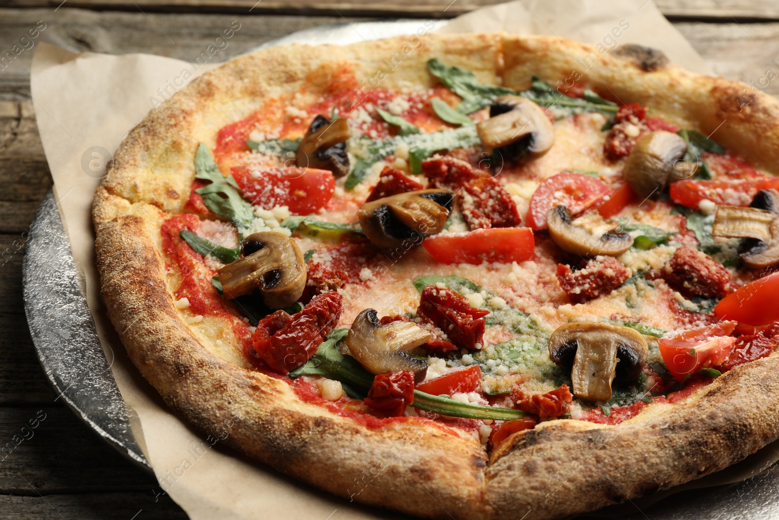 Photo of Tasty pizza with mushrooms, tomatoes and arugula on wooden table, closeup