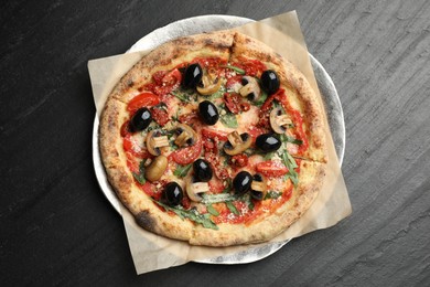 Tasty pizza with mushrooms, olives and arugula on black table, top view