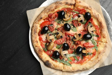 Photo of Tasty pizza with mushrooms, olives and arugula on black table, top view