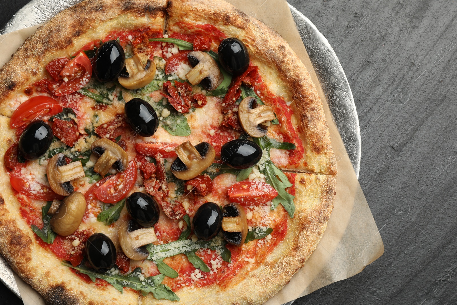 Photo of Tasty pizza with mushrooms, olives and arugula on black table, top view