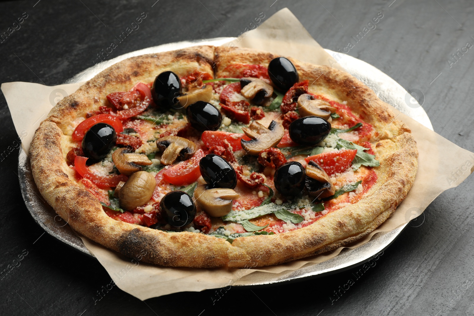 Photo of Tasty pizza with mushrooms, olives and arugula on black table, closeup