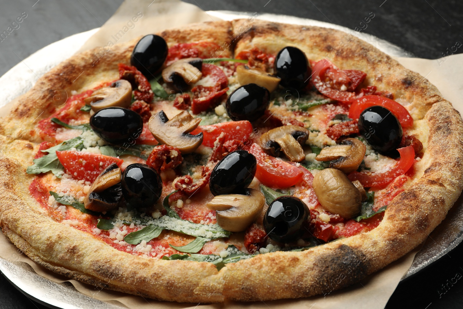 Photo of Tasty pizza with mushrooms, olives and arugula on black table, closeup