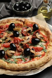 Tasty pizza with mushrooms, olives and arugula on black table, closeup