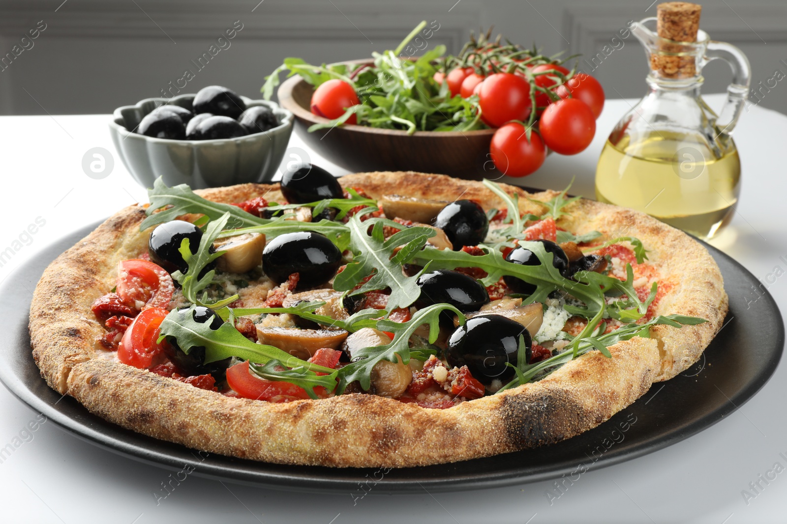 Photo of Tasty pizza with mushrooms, black olives, arugula and tomatoes on white table, closeup