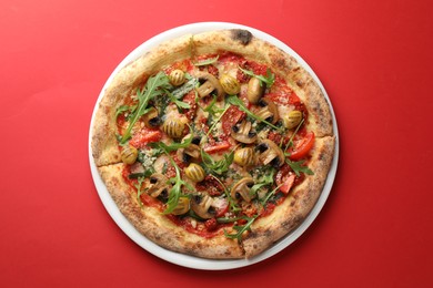 Photo of Tasty pizza with mushrooms, olives and arugula on red background, top view