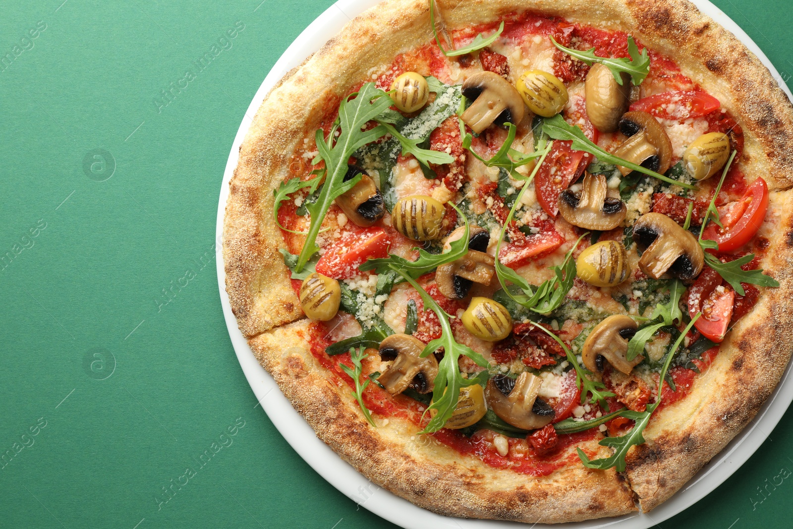 Photo of Tasty pizza with mushrooms, olives and arugula on green background, top view. Space for text