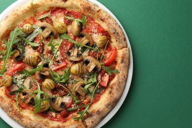 Photo of Tasty pizza with mushrooms, olives and arugula on green background, top view. Space for text