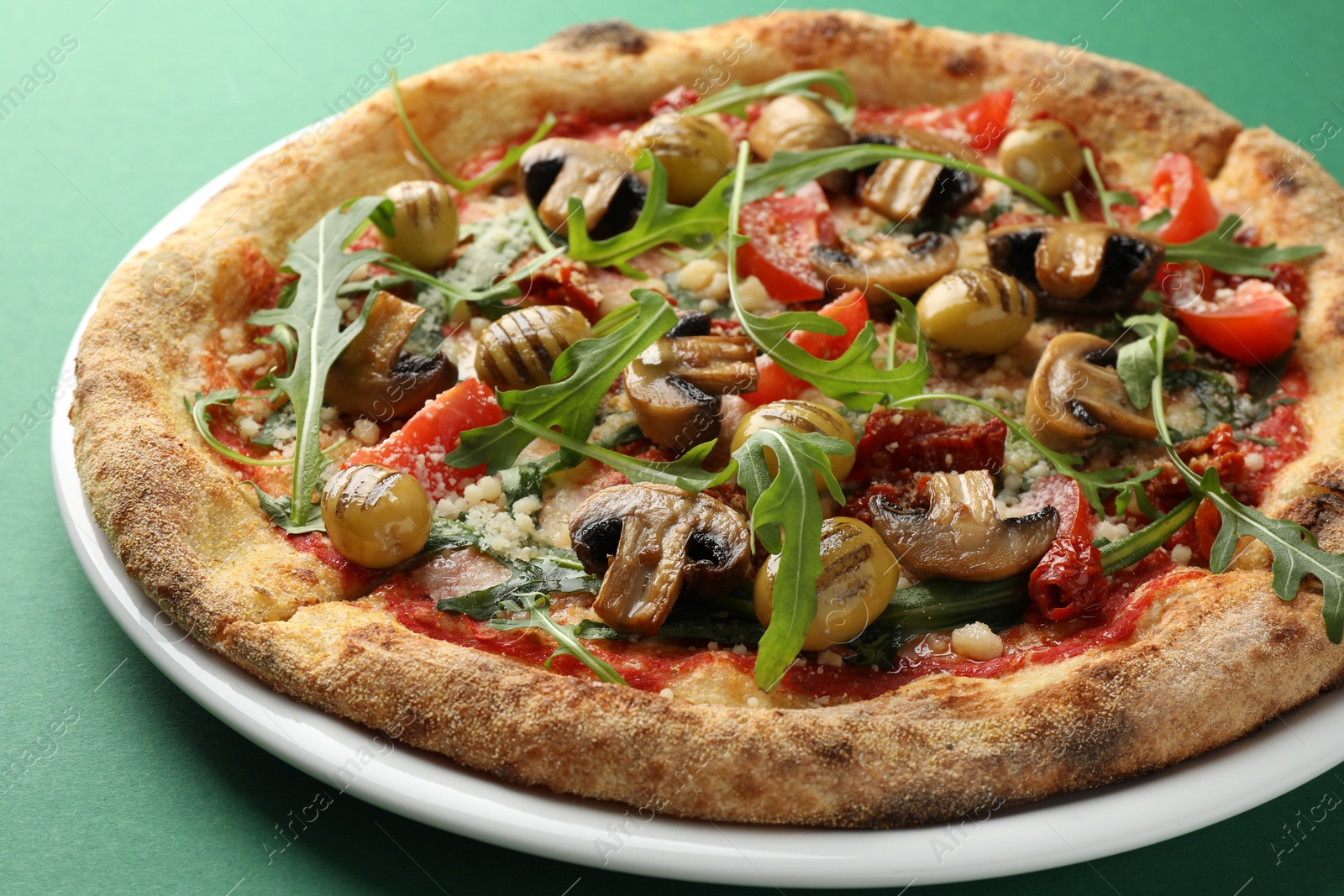 Photo of Tasty pizza with mushrooms, olives and arugula on green background, closeup