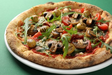 Photo of Tasty pizza with mushrooms, olives and arugula on green background, closeup