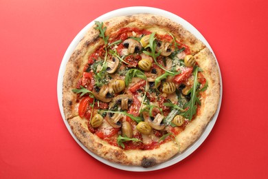 Photo of Tasty pizza with mushrooms, olives and arugula on red background, top view