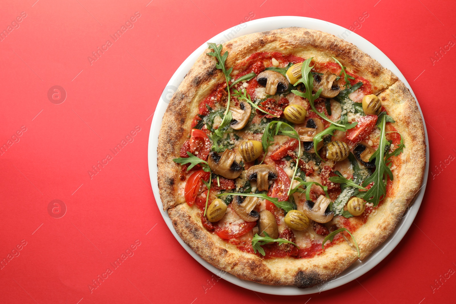 Photo of Tasty pizza with mushrooms, olives and arugula on red background, top view. Space for text