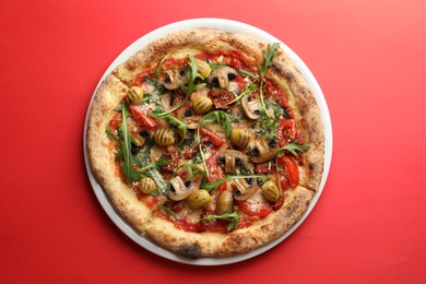 Photo of Tasty pizza with mushrooms, olives and arugula on red background, top view