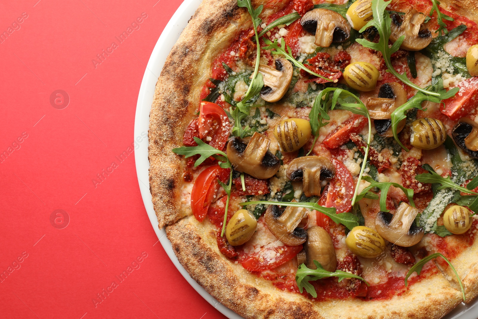 Photo of Tasty pizza with mushrooms, olives and arugula on red background, top view. Space for text