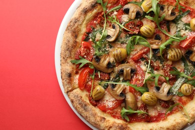 Tasty pizza with mushrooms, olives and arugula on red background, top view. Space for text