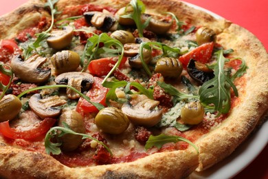 Tasty pizza with mushrooms, olives and arugula on red background, closeup