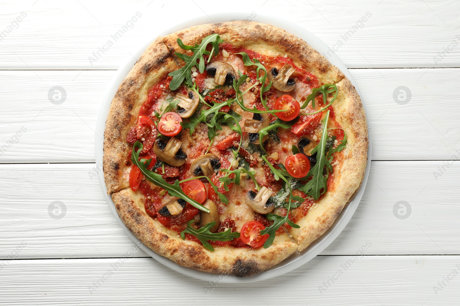 Photo of Tasty pizza with mushrooms, tomatoes and arugula on white wooden table, top view