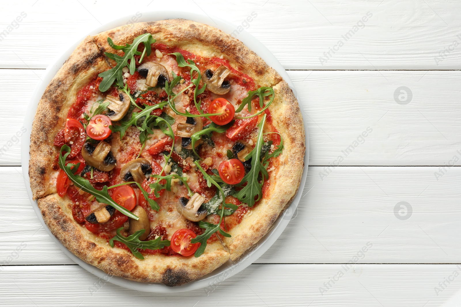 Photo of Tasty pizza with mushrooms, tomatoes and arugula on white wooden table, top view. Space for text