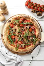 Photo of Tasty pizza with mushrooms, tomatoes, arugula and server on white wooden table, flat lay