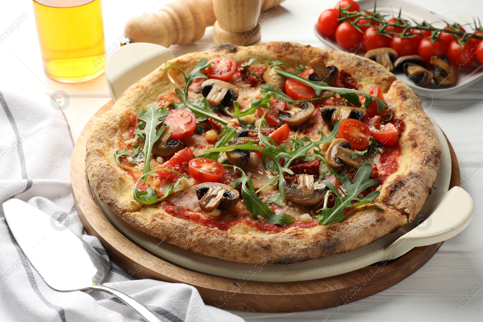 Photo of Tasty pizza with mushrooms, tomatoes and arugula on white wooden table, closeup