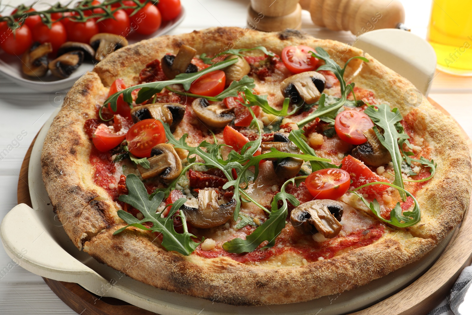 Photo of Tasty pizza with mushrooms, tomatoes and arugula on white wooden table, closeup