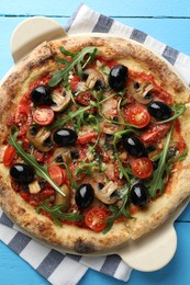 Photo of Tasty pizza with mushrooms, black olives and arugula on light blue wooden table, top view