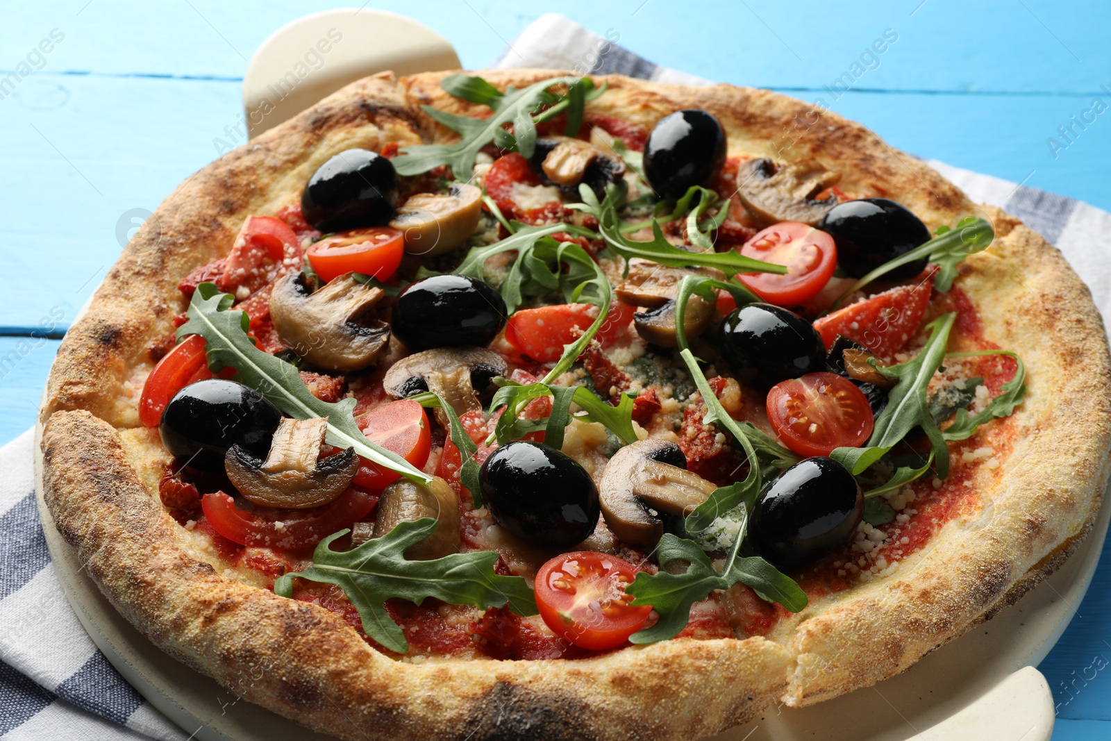 Photo of Tasty pizza with mushrooms, black olives and arugula on light blue wooden table, closeup