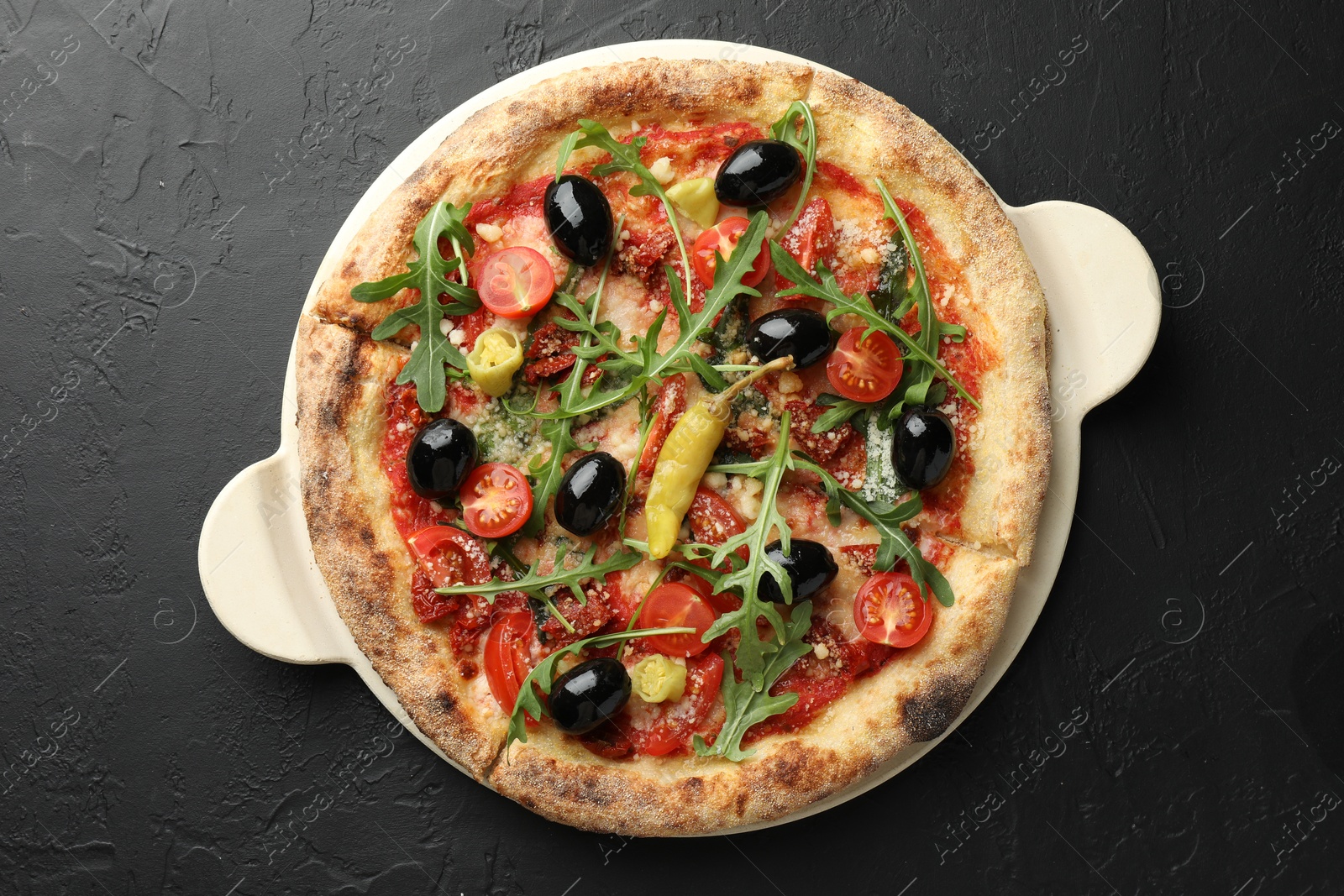 Photo of Tasty pizza with tomatoes, olives, chili and arugula on black table, top view