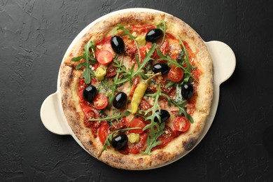 Tasty pizza with tomatoes, olives, chili and arugula on black table, top view