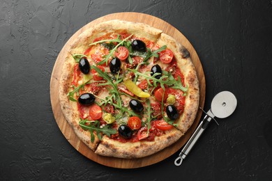 Photo of Tasty pizza with tomatoes, olives, chili and cutter on black table, top view