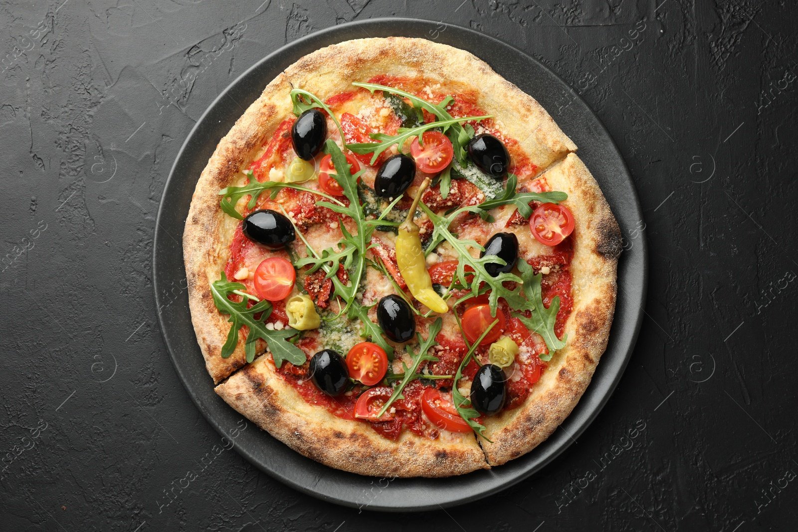 Photo of Tasty pizza with tomatoes, olives, chili and arugula on black table, top view