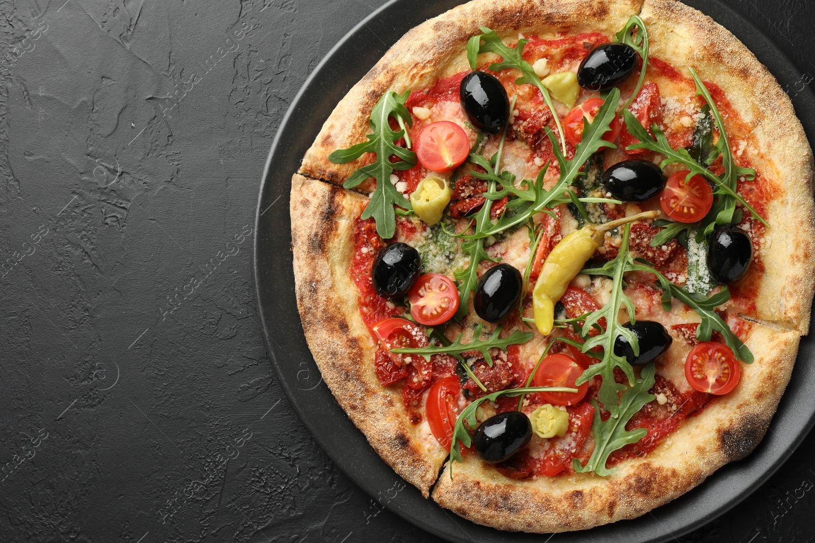 Photo of Tasty pizza with tomatoes, olives, chili and arugula on black table, top view. Space for text