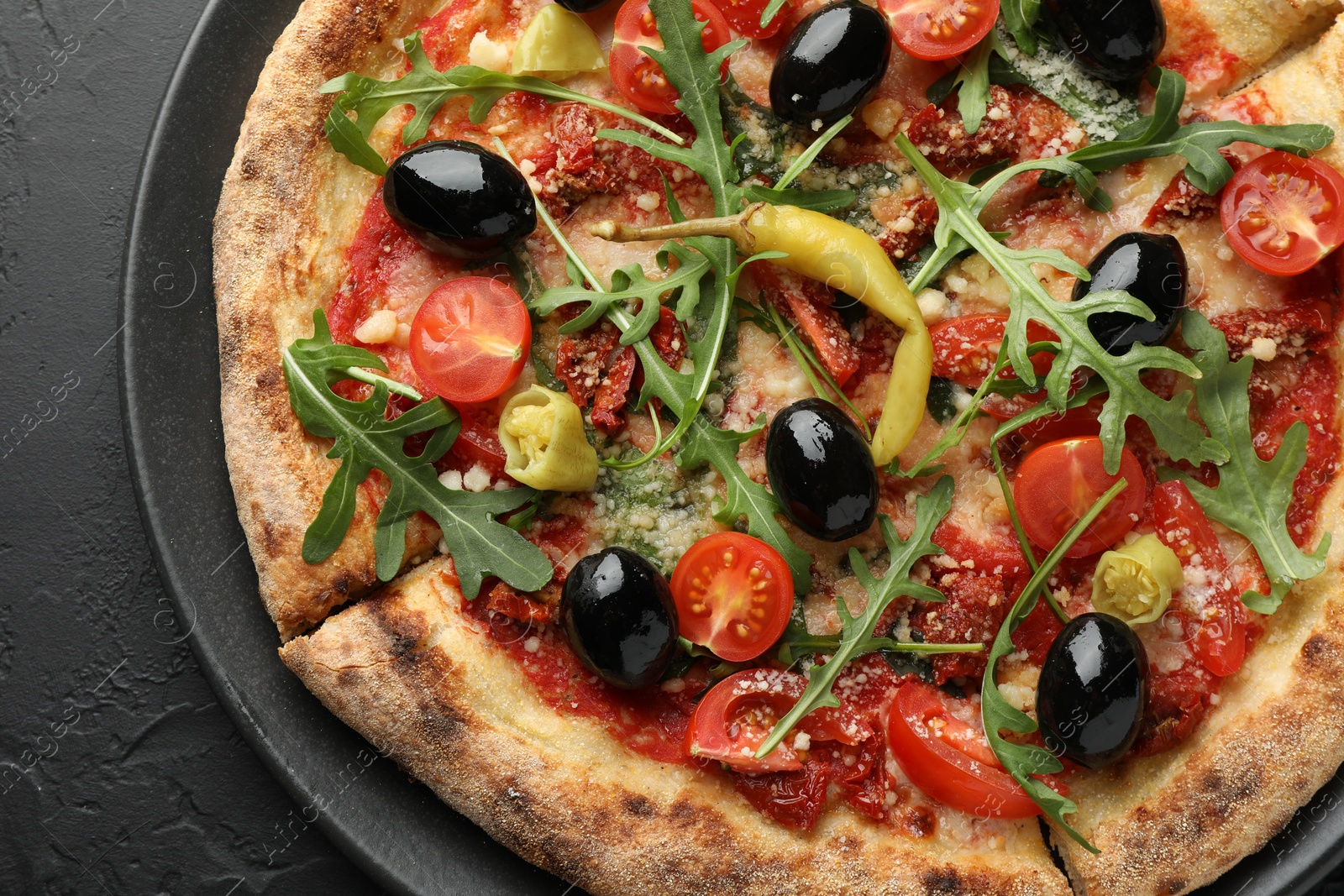 Photo of Tasty pizza with tomatoes, olives, chili and arugula on black table, top view