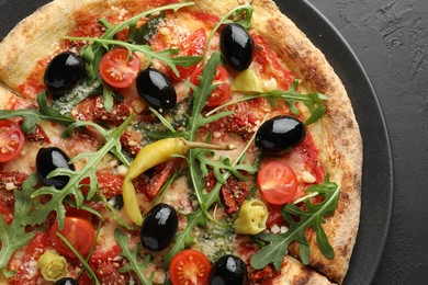 Tasty pizza with tomatoes, olives, chili and arugula on black table, top view