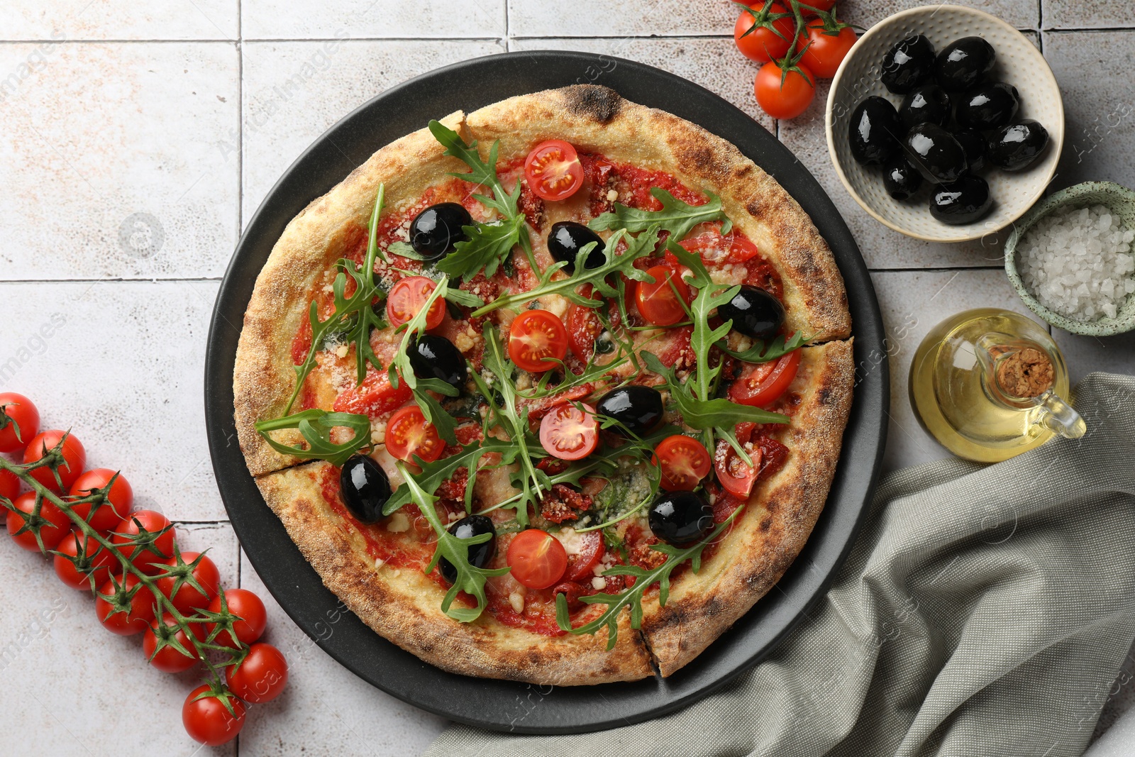 Photo of Tasty pizza with black olives, tomatoes and arugula served on light tiled table, flat lay