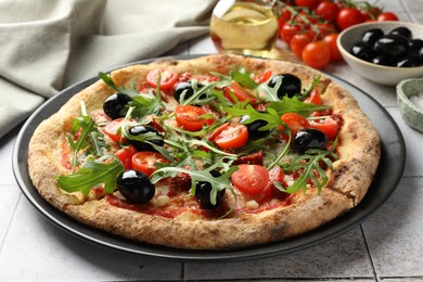 Tasty pizza with tomatoes, olives and arugula on light tiled table, closeup