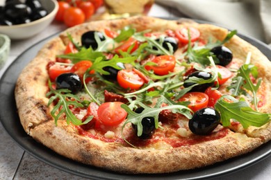 Tasty pizza with tomatoes, olives and arugula on light tiled table, closeup