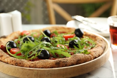 Delicious pizza with olives, cherry tomatoes and arugula on table indoors, closeup