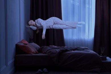 Image of Sleepwalking. Young woman floating above bed at home