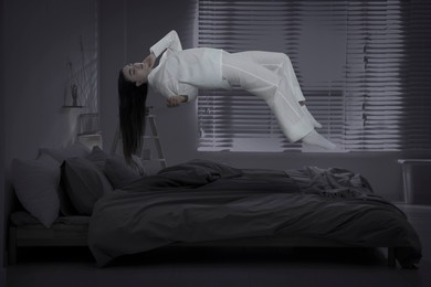 Sleepwalking. Young woman floating over bed at home. Black-and-white