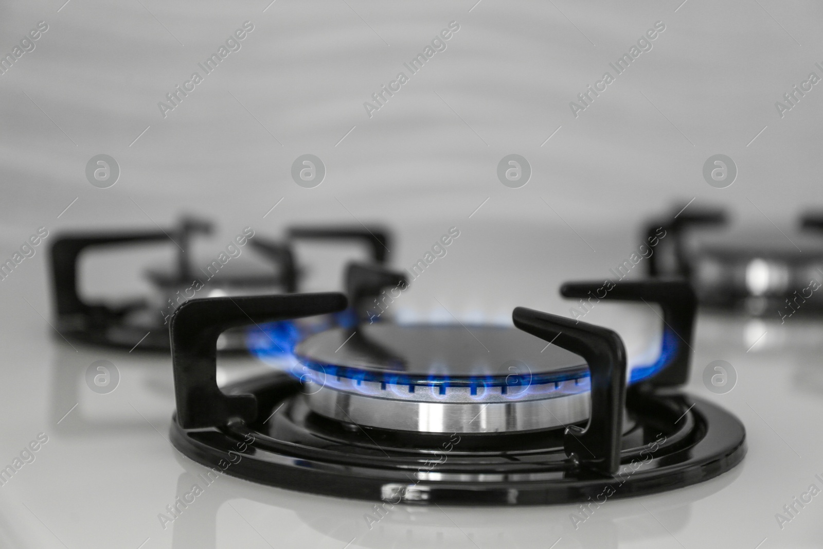 Photo of Gas burner of modern stove with burning blue flame, closeup