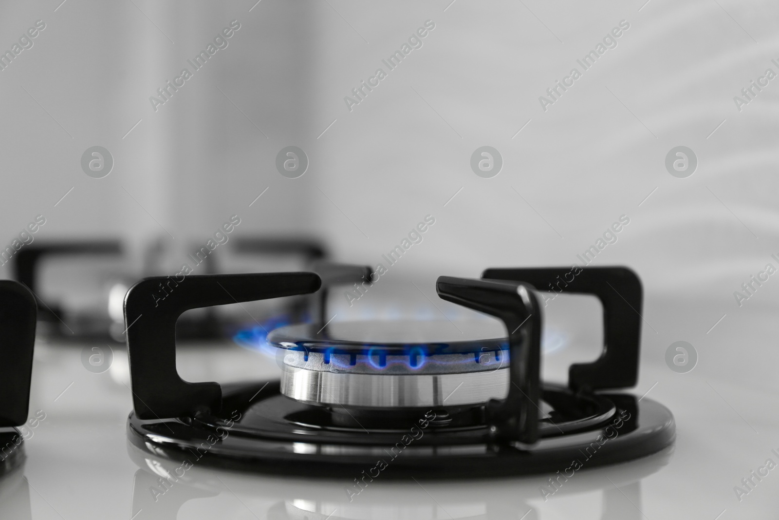 Photo of Gas burner of modern stove with burning blue flame, closeup