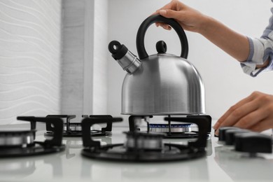 Photo of Woman putting kettle on gas stove in kitchen, closeup