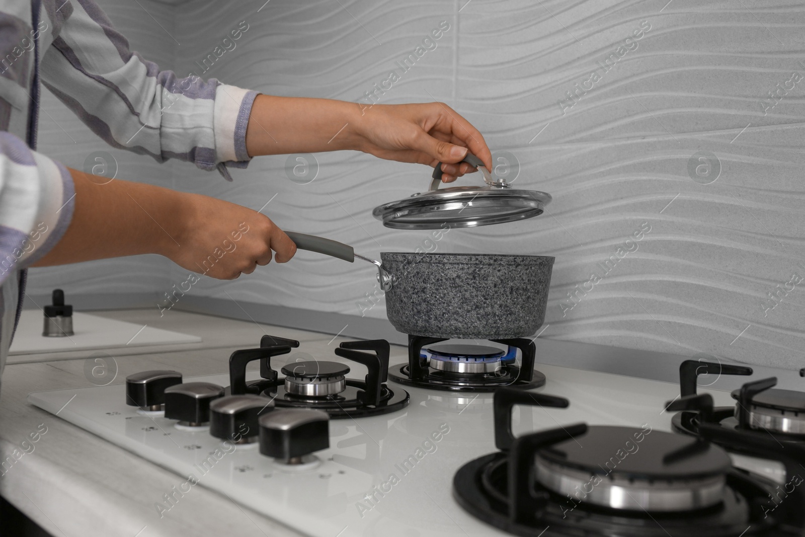 Photo of Woman putting pot on gas stove in kitchen, closeup