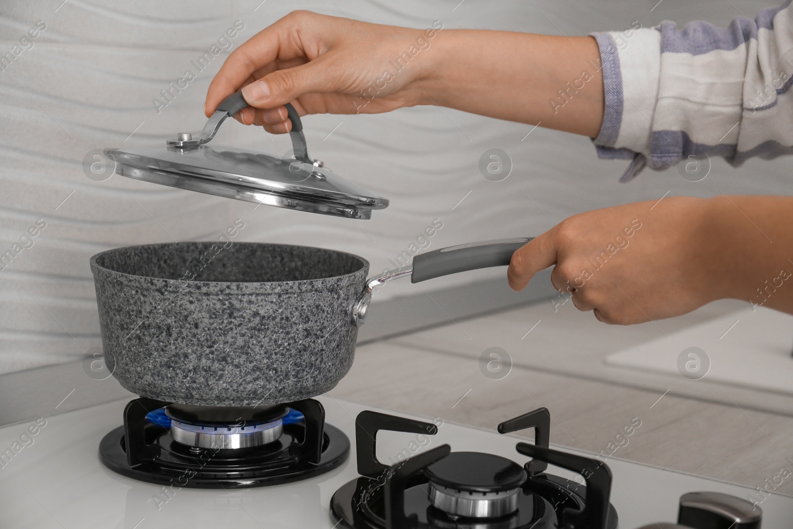 Photo of Woman putting pot on gas stove in kitchen, closeup