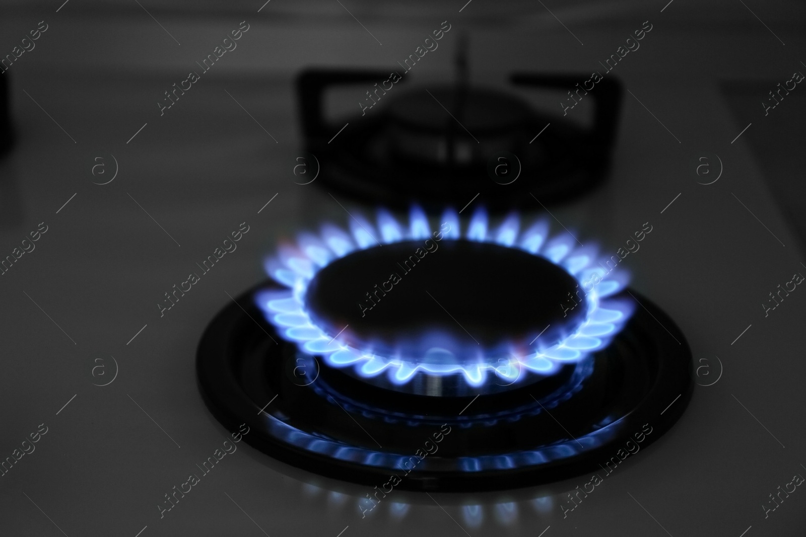 Photo of Modern gas cooktop with burning blue flame in kitchen at night