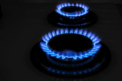 Photo of Modern gas cooktop with burning blue flames in kitchen at night