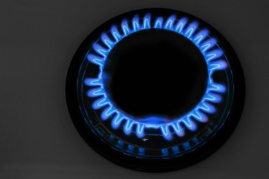 Photo of Gas burner of modern stove with burning blue flame at night, closeup