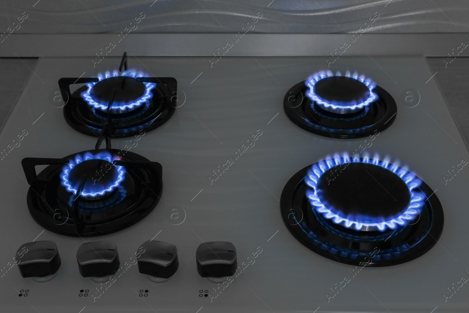 Photo of Modern gas cooktop with burning blue flames in kitchen